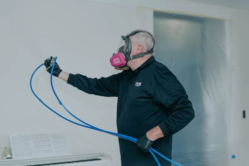 Technician in respirator applying dry fog treatment through hoses in a room being remediated